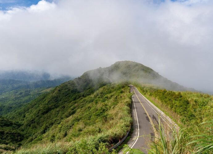 A winding road through lush green hills under a cloudy sky.