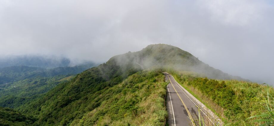 A winding road through lush green hills under a cloudy sky.